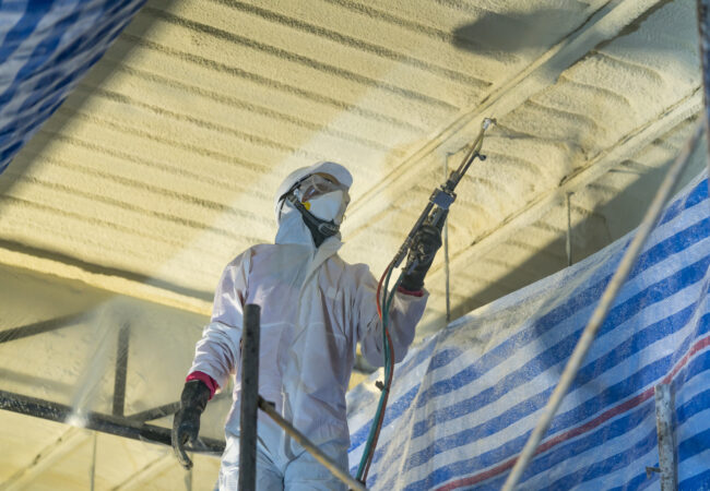 Technician spraying foam insulation using Plural Component Gun f Spray foam in warehouse