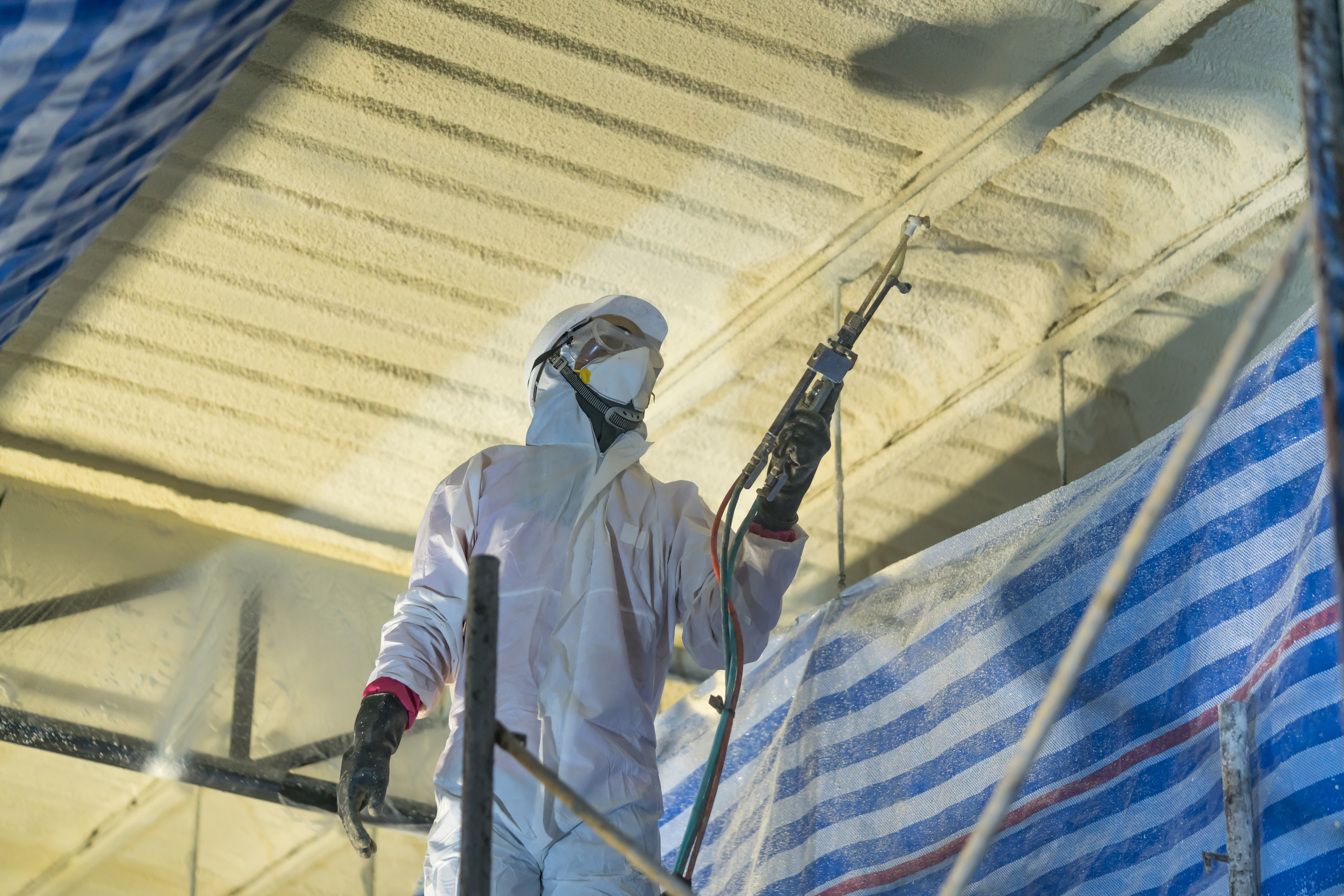 Technician spraying foam insulation using Plural Component Gun f Spray foam in warehouse